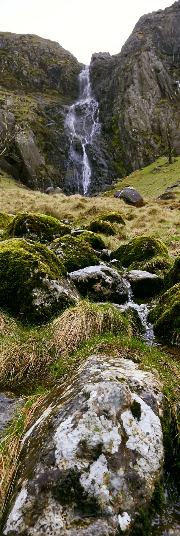 Mossy boulder meadow with waterfall in rocky landscape - AI-generated stock image