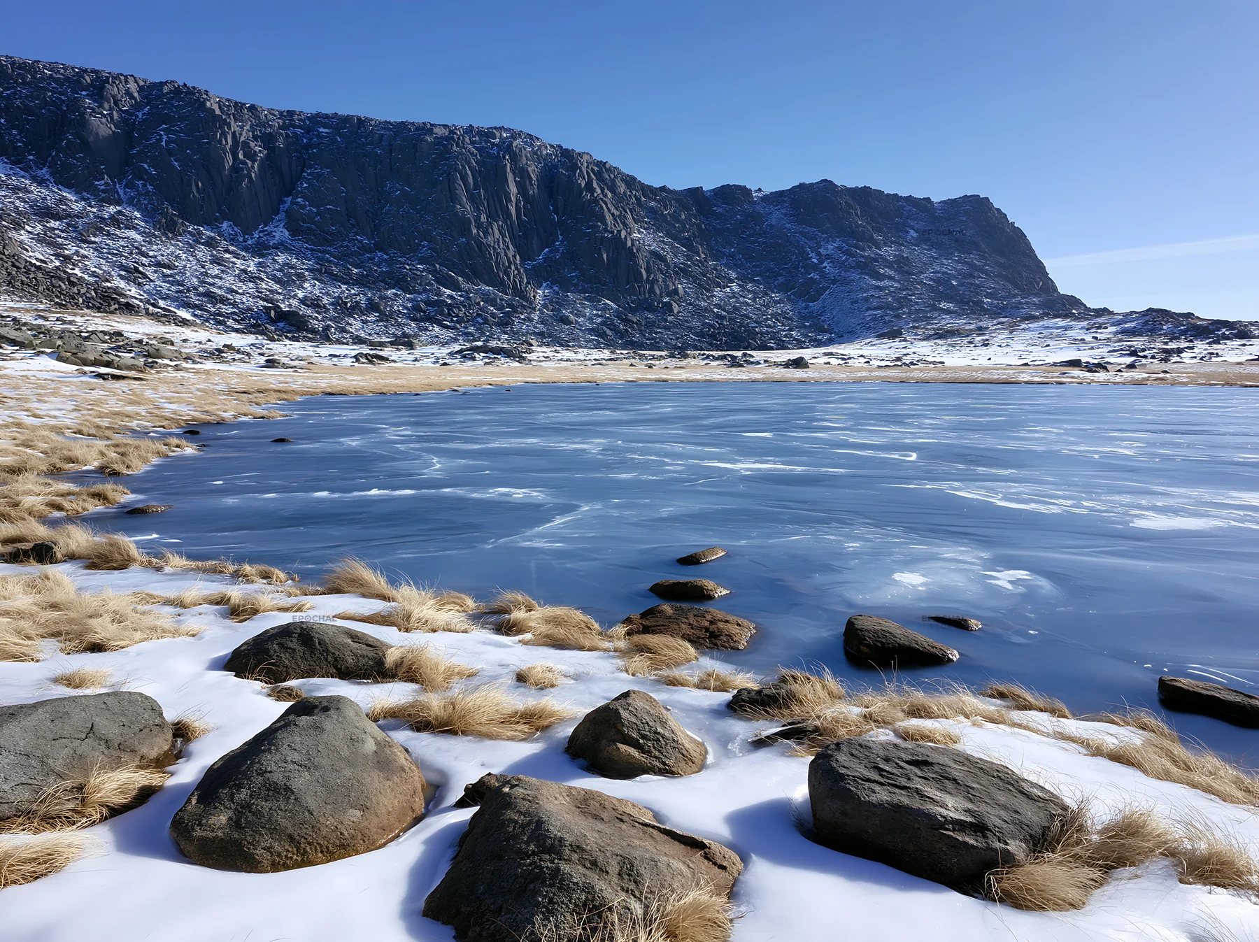 Frozen tarn in a meadow surrounded by rocks and mountains - AI-generated stock image