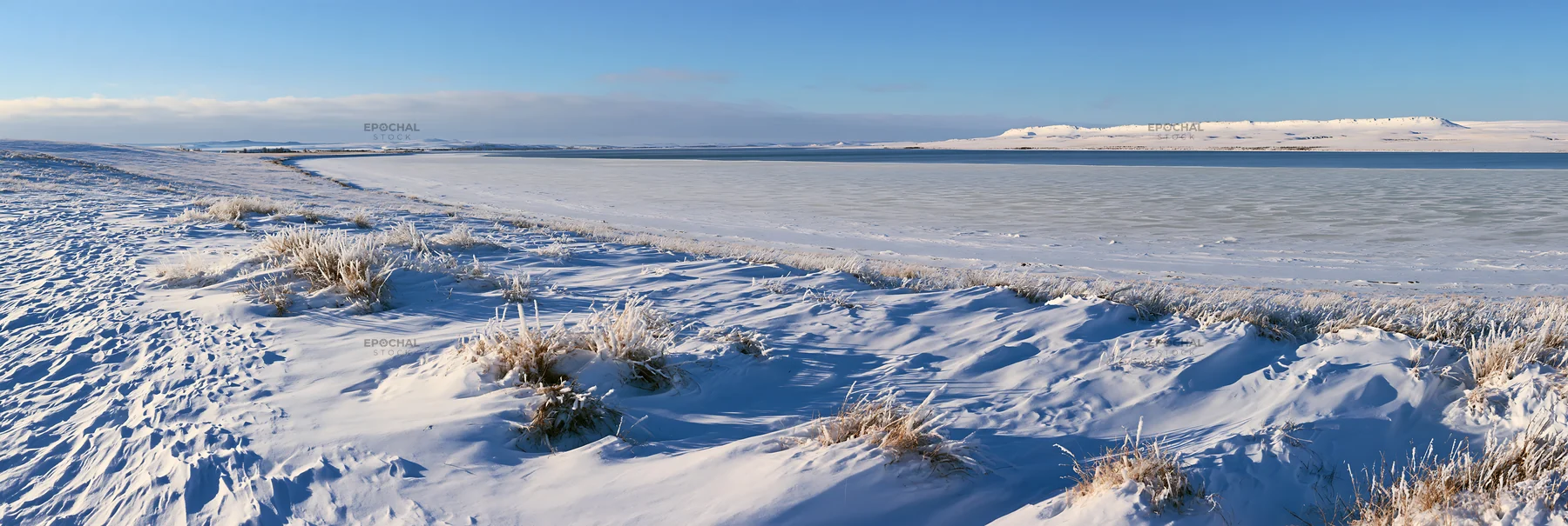 Snowy lakeside meadow with frozen lake and clear sky - AI-generated stock image