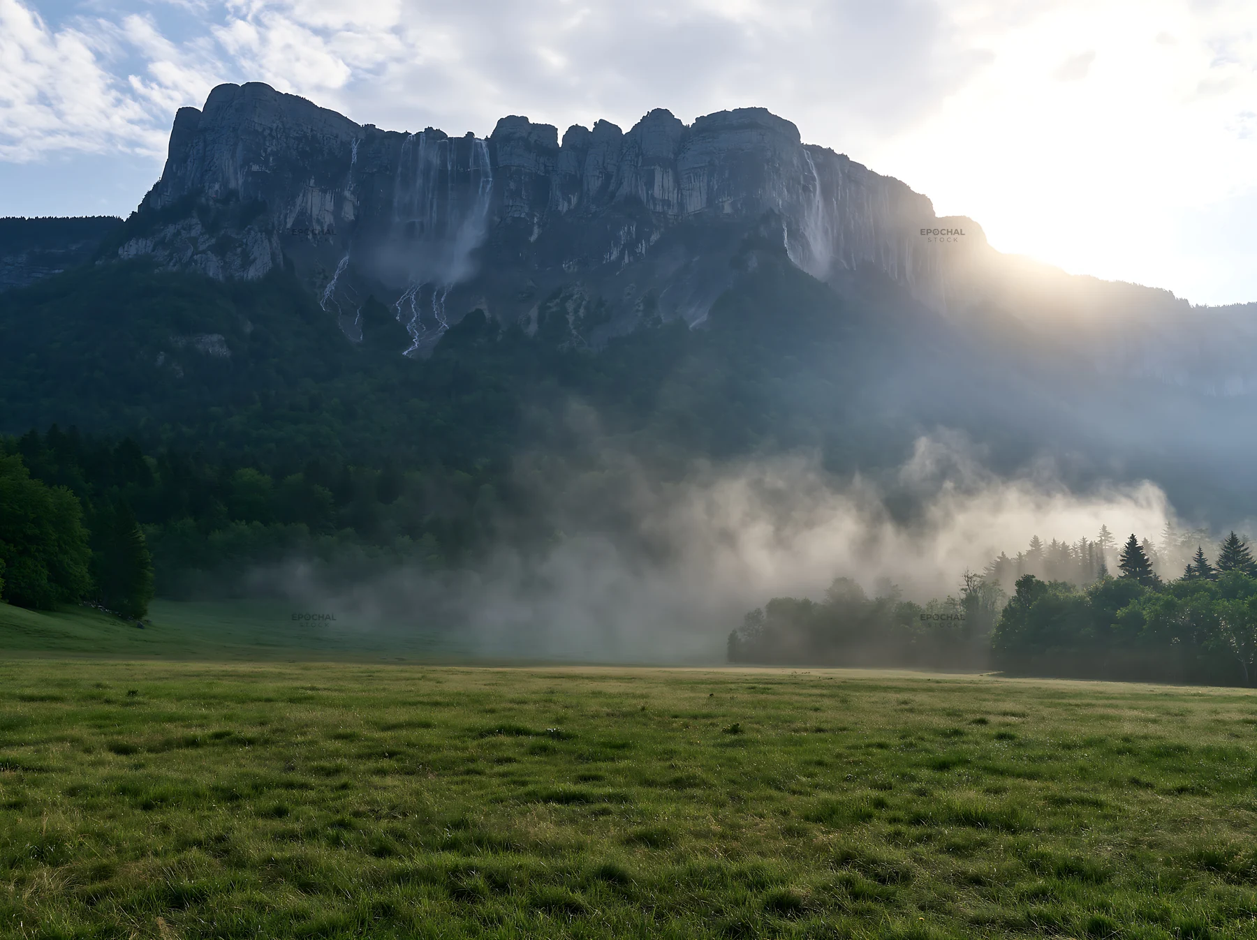 Meadow beneath crags with mist in morning light - AI-generated stock image