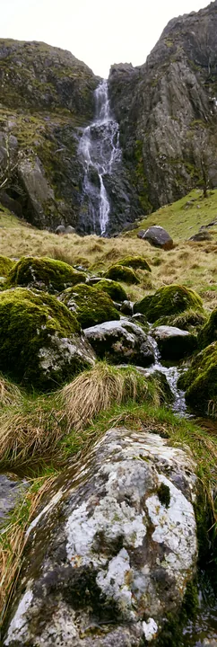 Mossy boulder meadow with waterfall in rocky landscape - AI-generated stock image