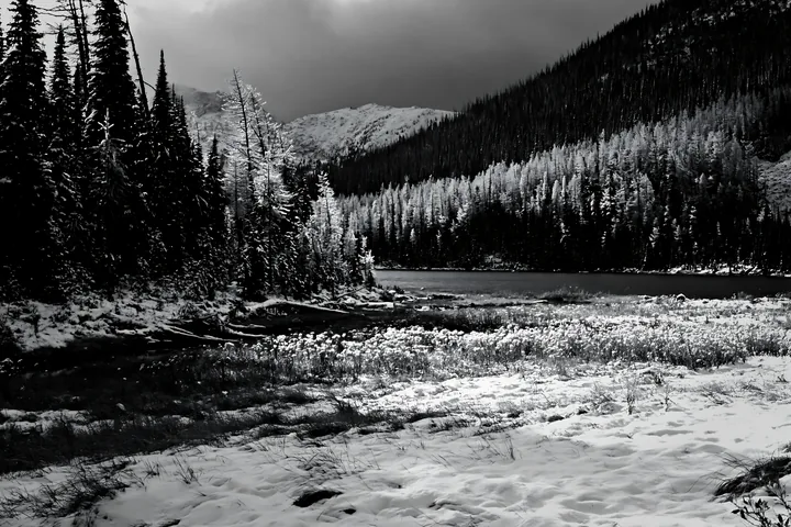 Lakeside meadow after snowfall in a mountain landscape - AI-generated stock image