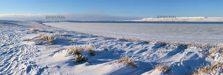 Snowy lakeside meadow with frozen lake and clear sky - AI-generated stock image