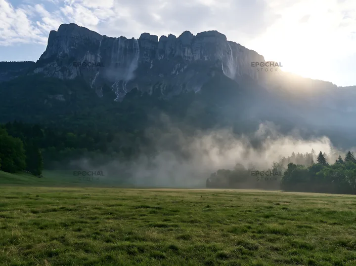 Meadow beneath crags with mist in morning light - AI-generated stock image