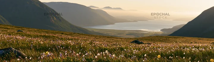 Meadow beneath crags with distant mountains and a wide river view - AI-generated stock image