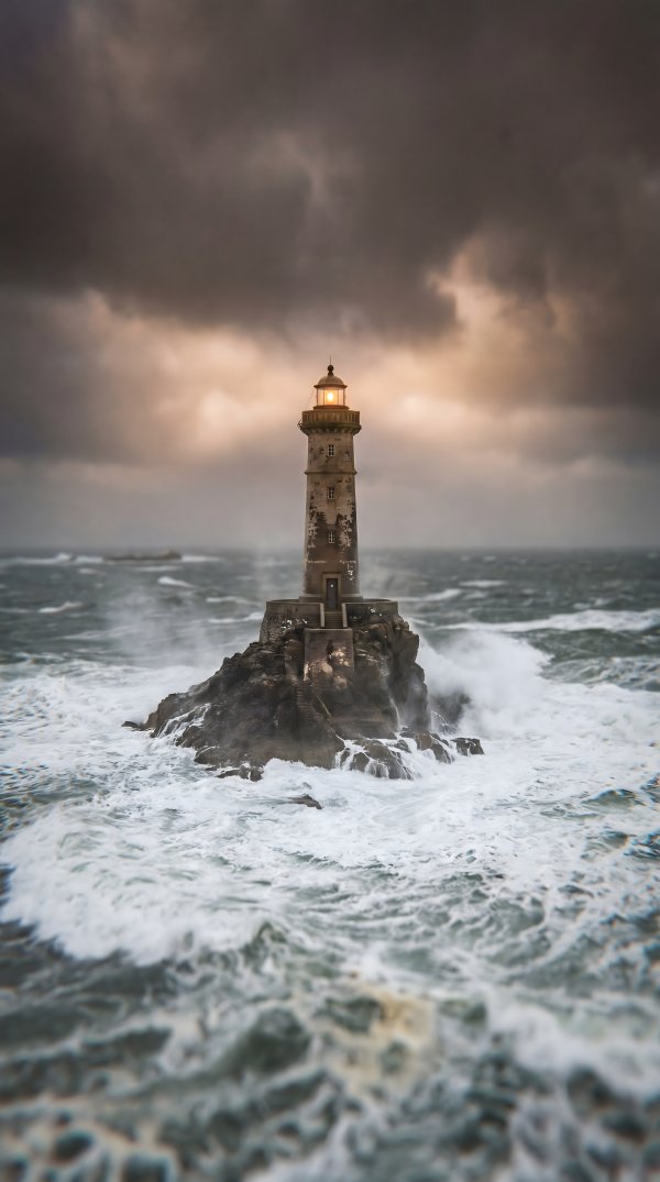 Lighthouse stands on rock during stormy weather at sunset - stock photo