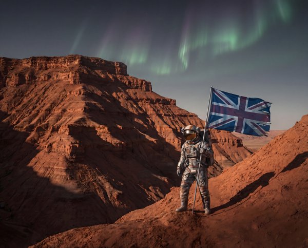 An astronaut holds a British flag while standing on rocky land - stock photo