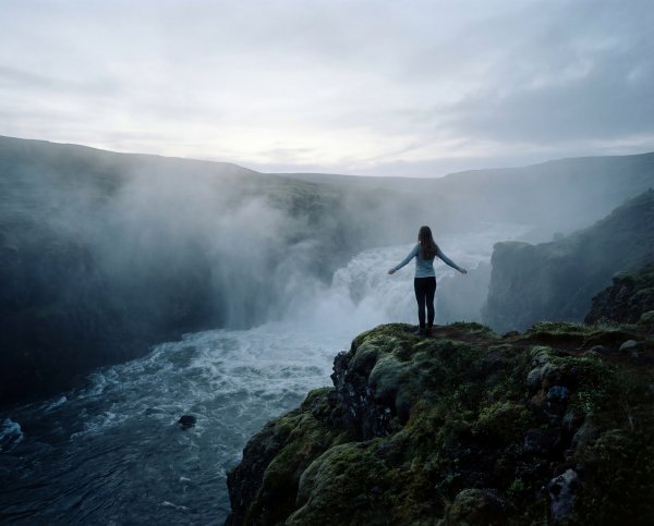 Person stands by waterfall in Iceland during cloudy weather - stock photo