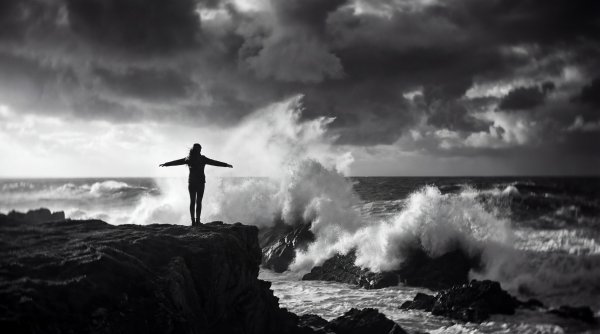 Person stands on rocks by ocean waves during storm - stock photo