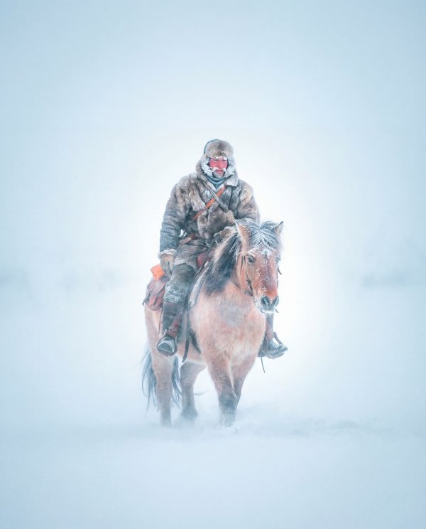 Man riding horse in snow during winter weather - stock photo