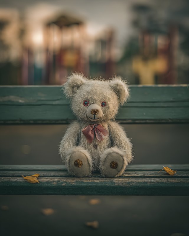 Teddy bear sits alone on a bench in a playground Free Premium Stock Photo - stock photo