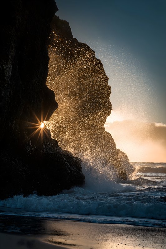 Sunlight shines through rocks while waves crash at shore Free Premium Stock Photo - stock photo