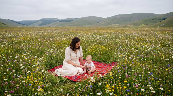 Mother and baby enjoy time in flower field near hills - stock photo