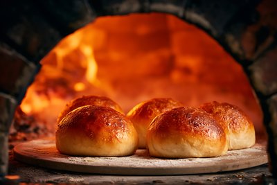 Freshly Baked Bierocks Emerging from Wood-Fired Oven in Warm Golden Light - stock photo