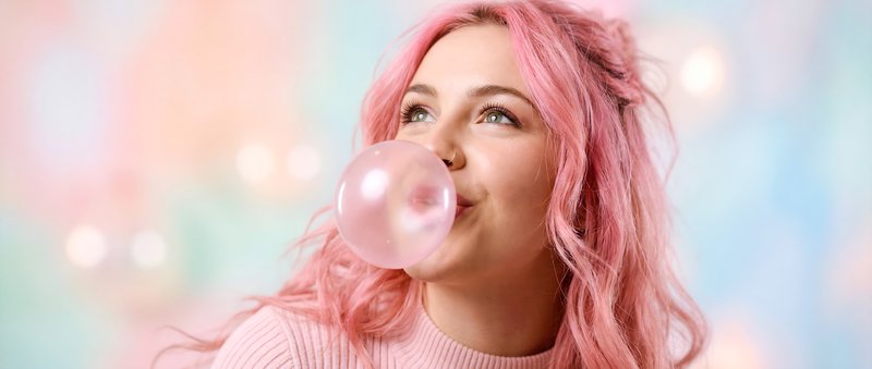 Girl blows pink bubble gum with colorful backdrop Premium Stock Photo - stock photo