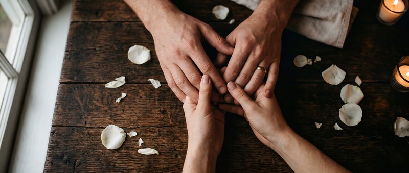 Hands joined together on a wooden table with petals and candles Premium Stock Image - stock photo