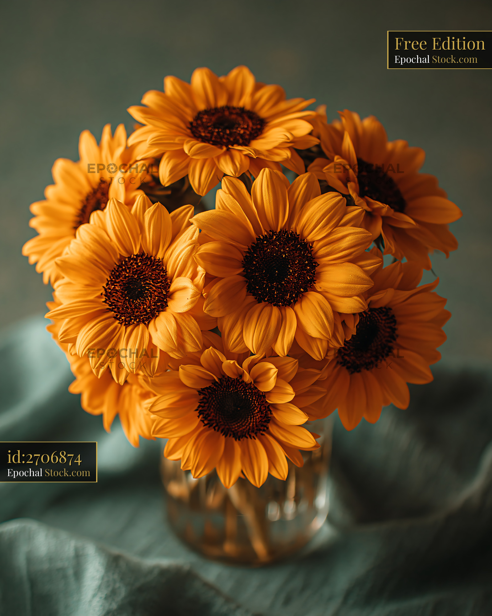 Vibrant sunflower bouquet in a glass vase on teal fabric - stock photo