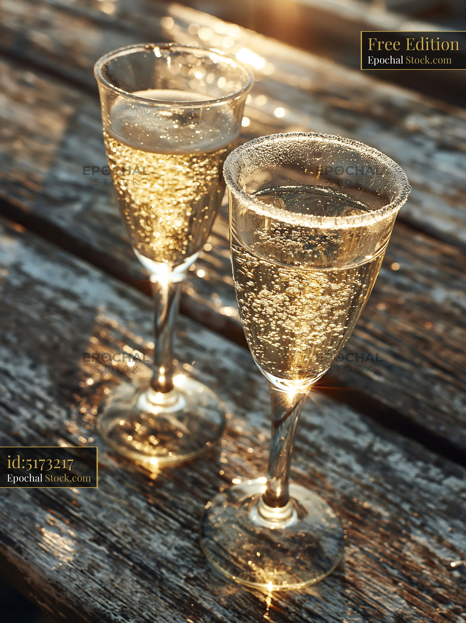 Two glasses of sparkling wine on a rustic wooden table at sunset - stock photo