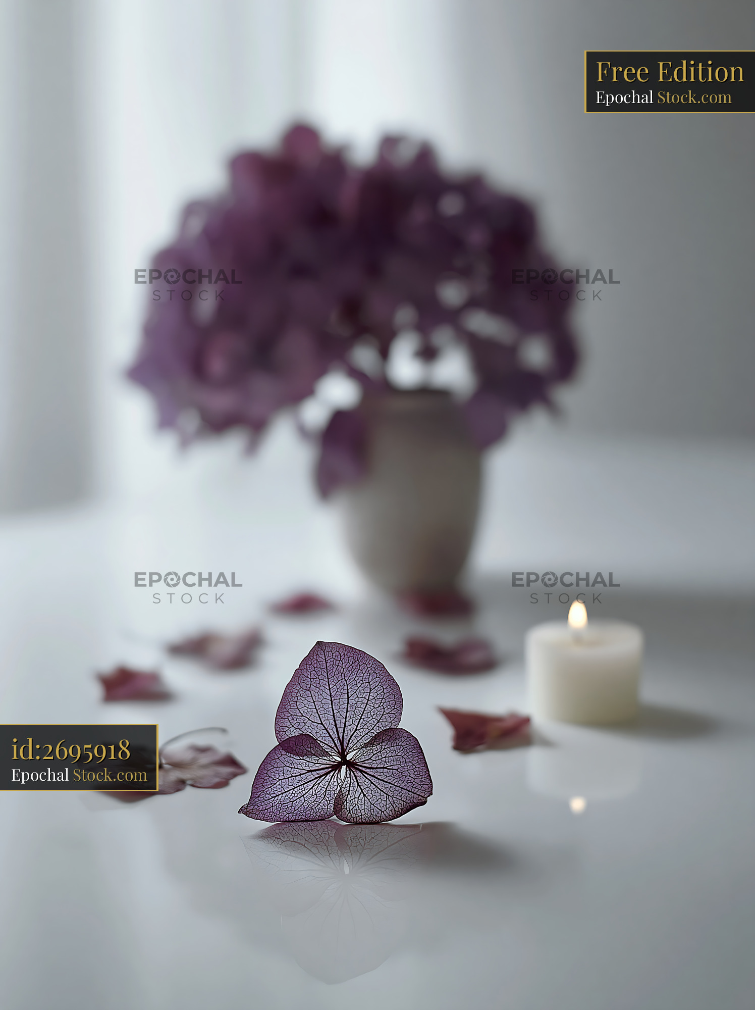 Dry hydrangea bouquet on a table with a lit candle and fallen petals - stock photo