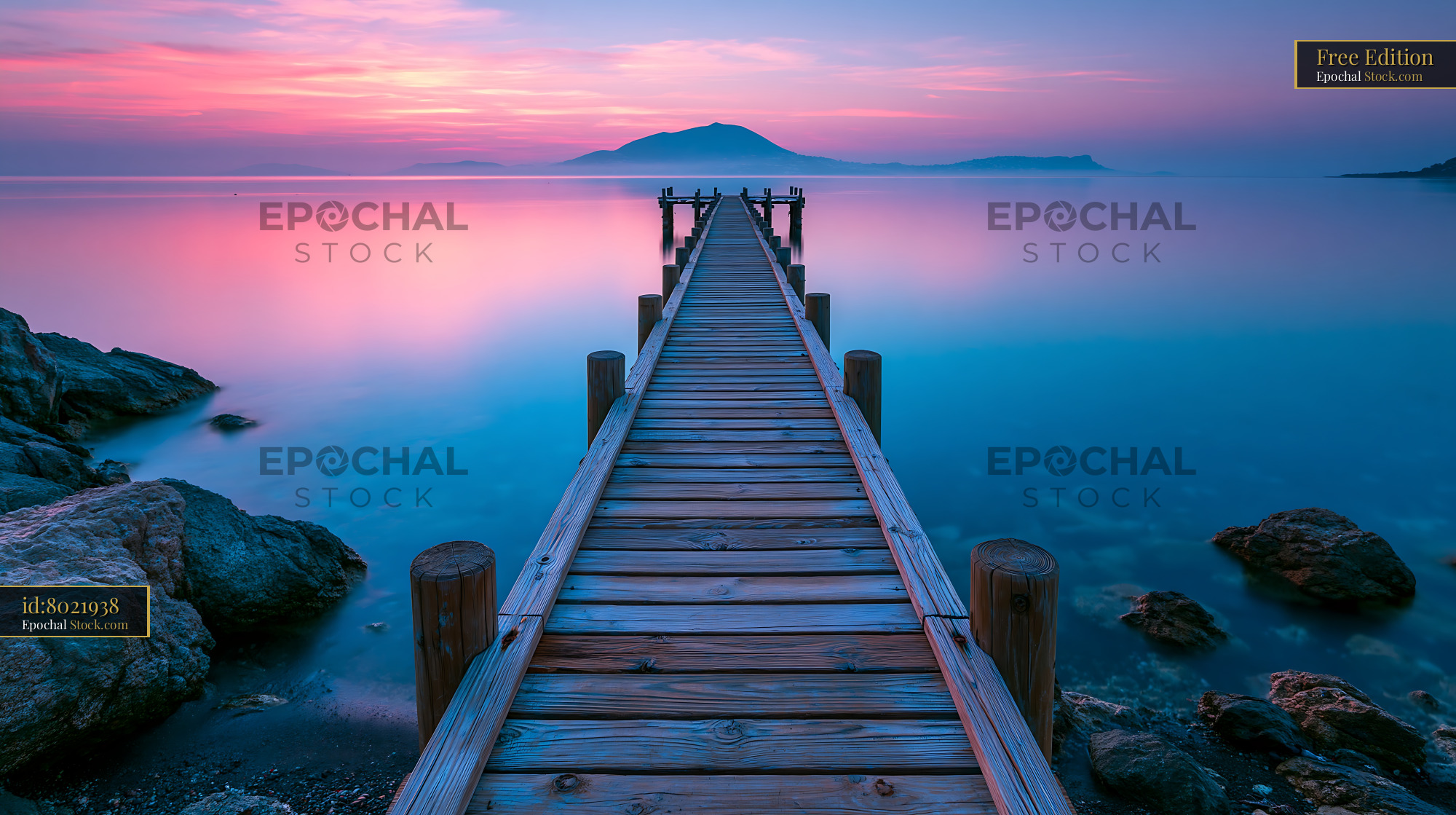 Wooden pier leading into calm water under vibrant sunset sky - stock photo