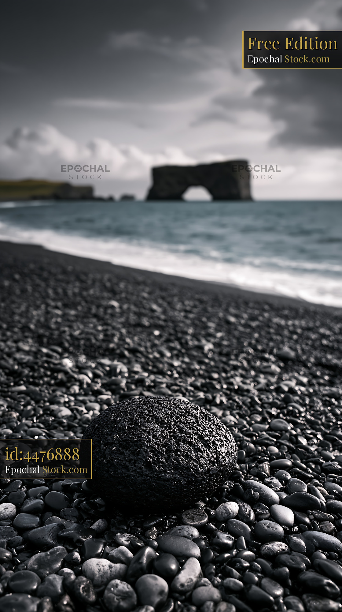 Single black volcanic stone on a moody pebble beach with rock arch - stock photo