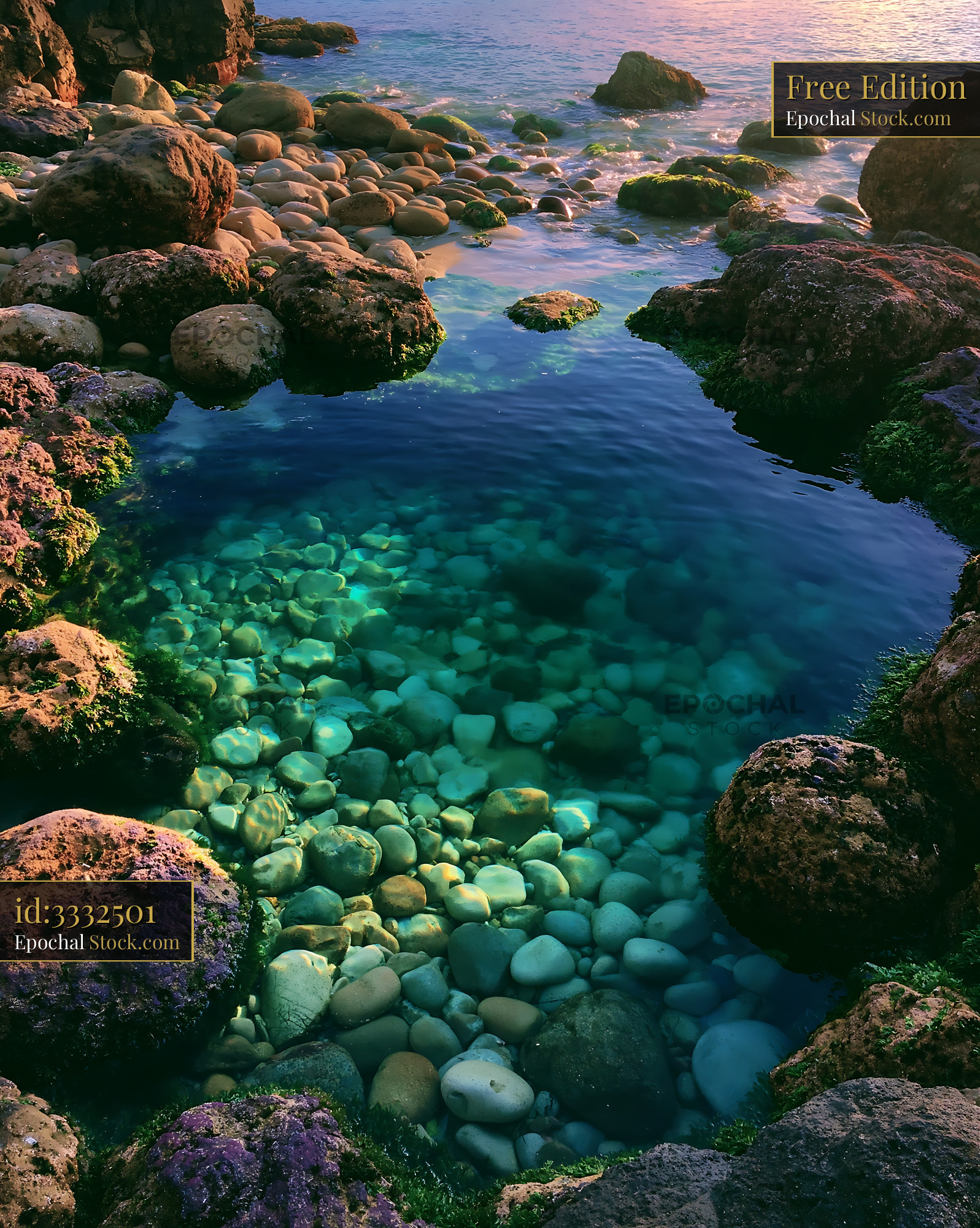 Clear tidepool with smooth pebbles at a rocky shore during golden hour - stock photo