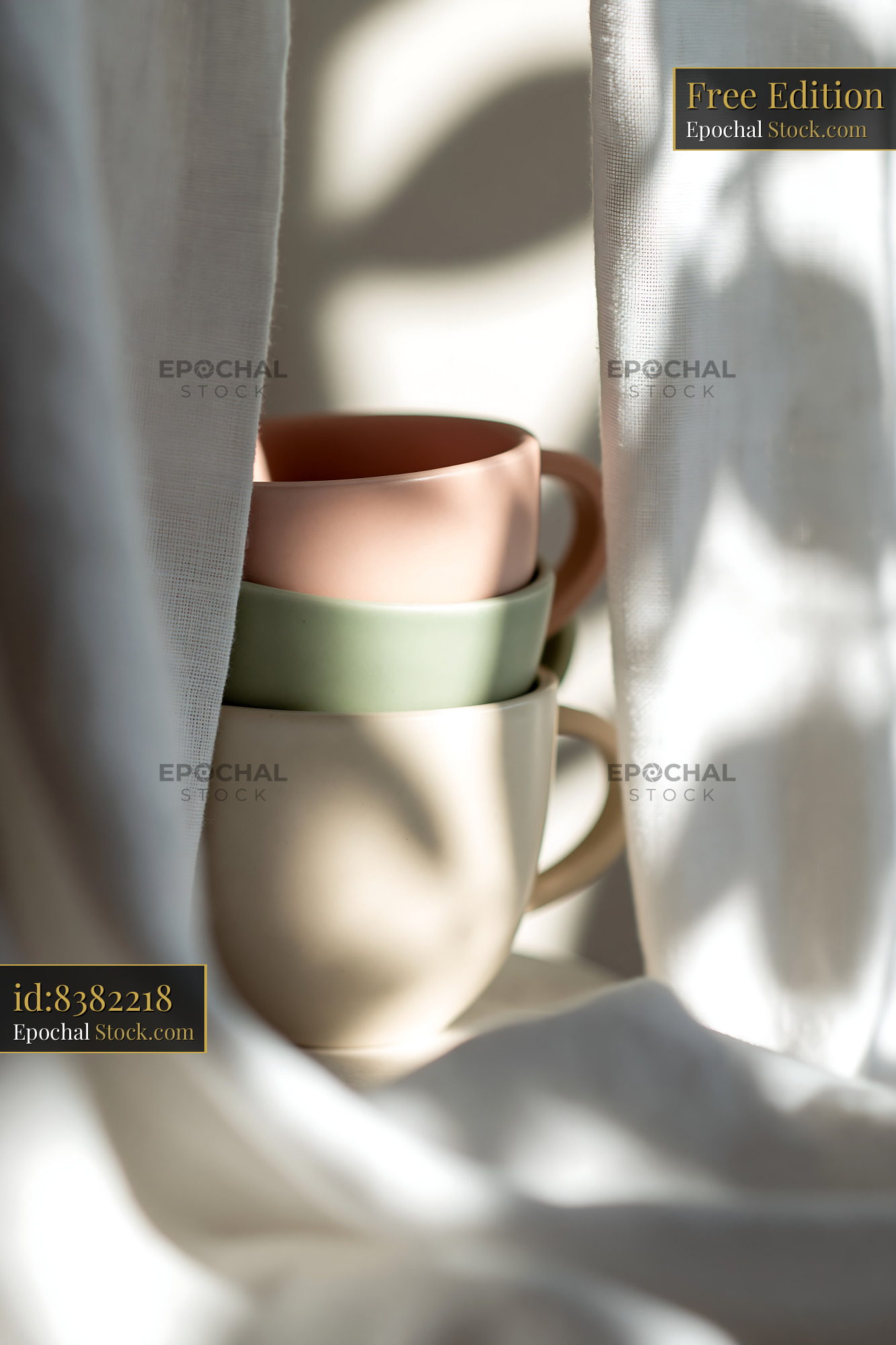 Stacked pastel ceramic mugs behind white curtains in morning light - stock photo