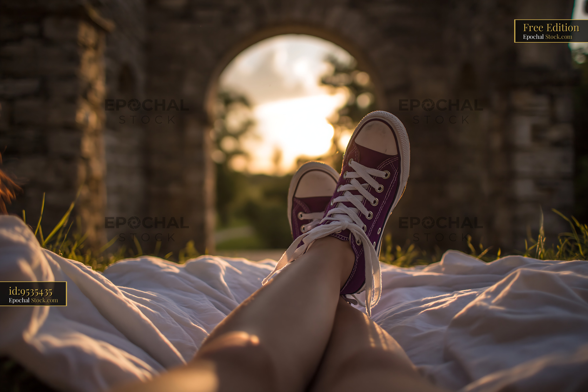 Young woman legs resting on grass with purple sneakers at sunset - stock photo