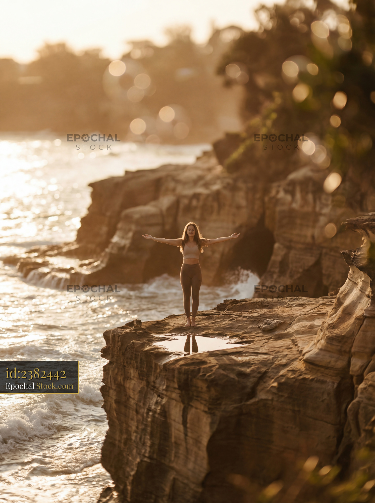 Woman stands on cliff by the ocean during sunset in warm light