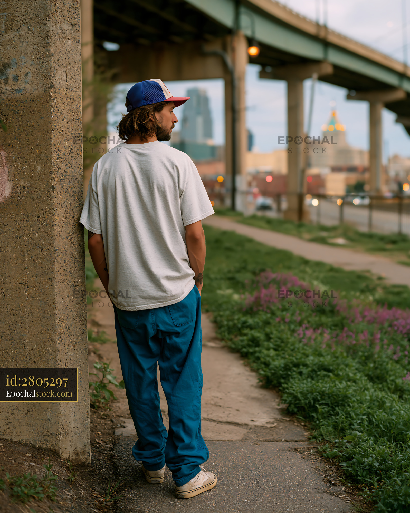 Watermarked full-resolution preview of Man standing near a concrete wall in urban setting at dusk