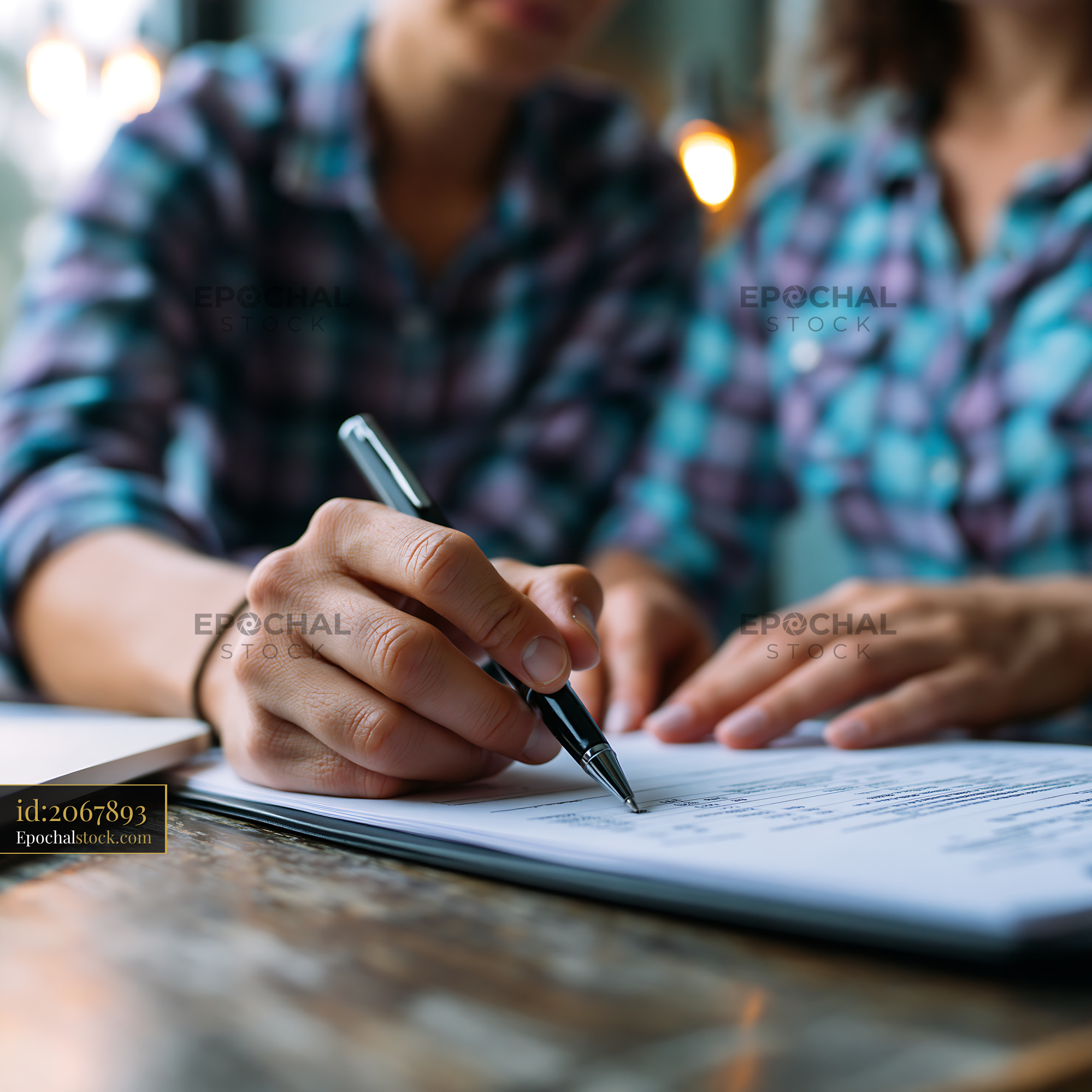 Watermarked full-resolution preview of Two people signing documents at a wooden table in a cafe