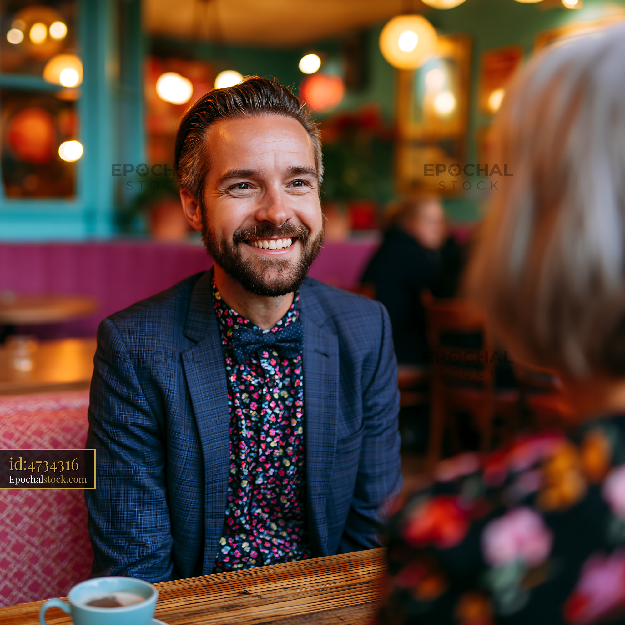 Watermarked full-resolution preview of Man smiles while sitting at a table in a cafe with a friend