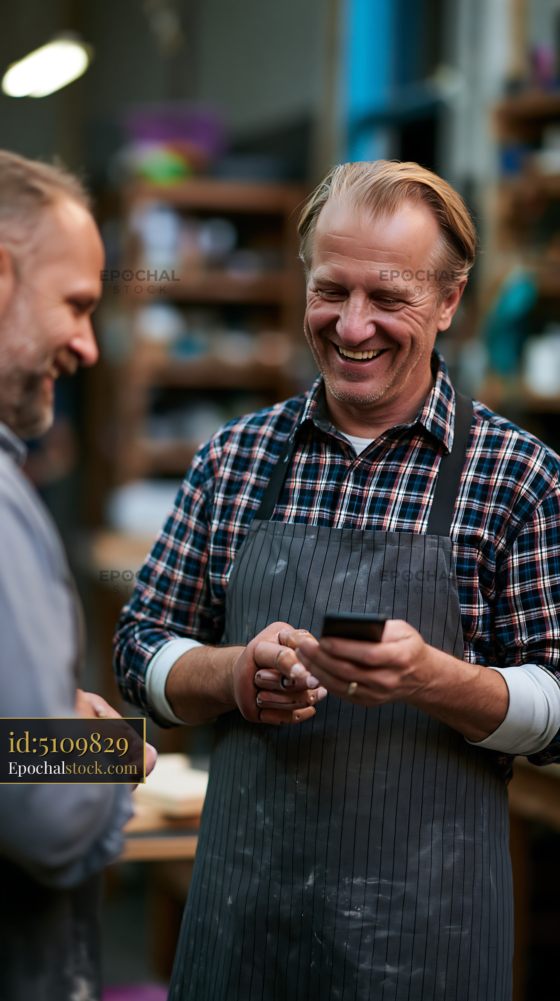 Watermarked full-resolution preview of Two men talking and smiling in a workshop setting