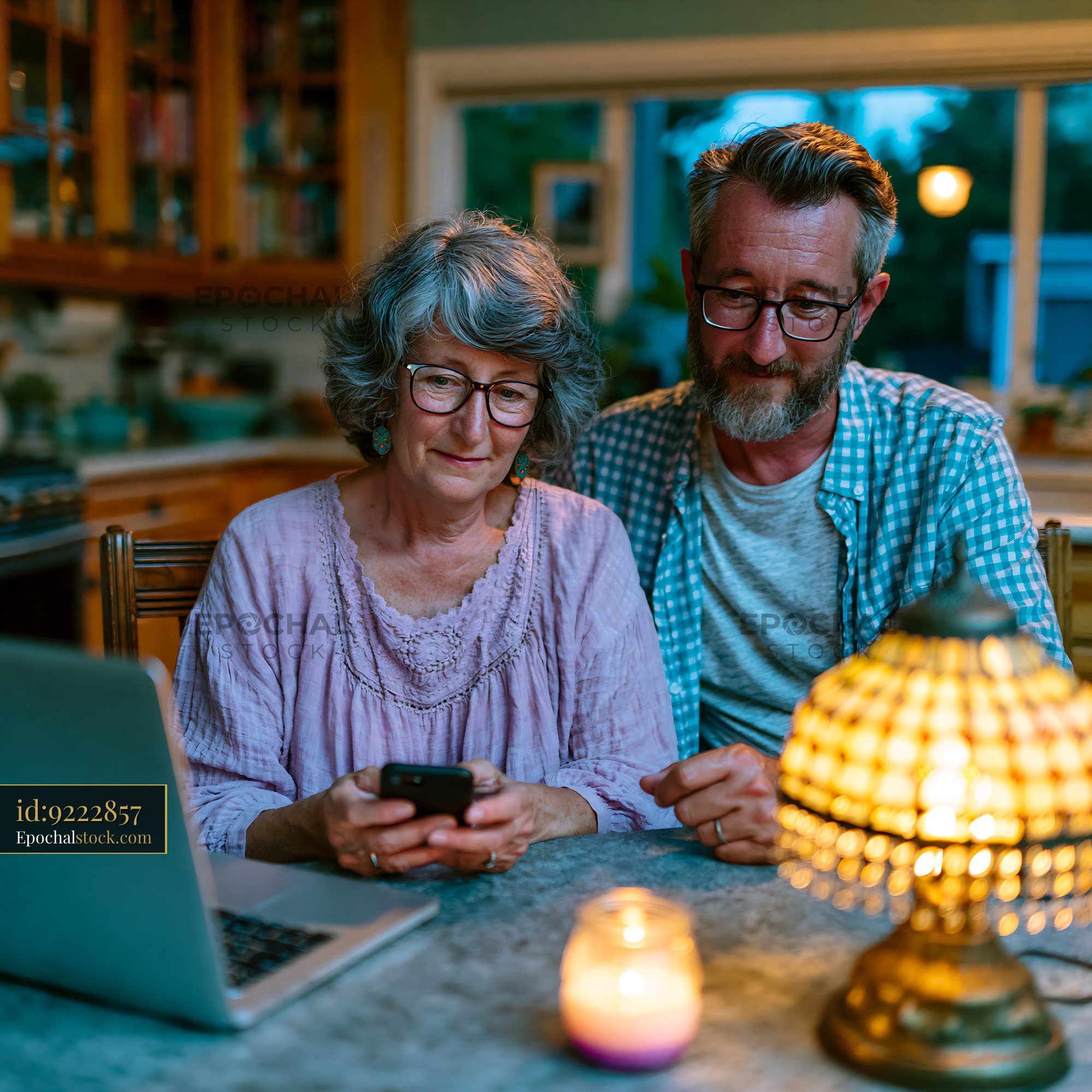 Watermarked full-resolution preview of Couple using smartphone and laptop at table in cozy home setting