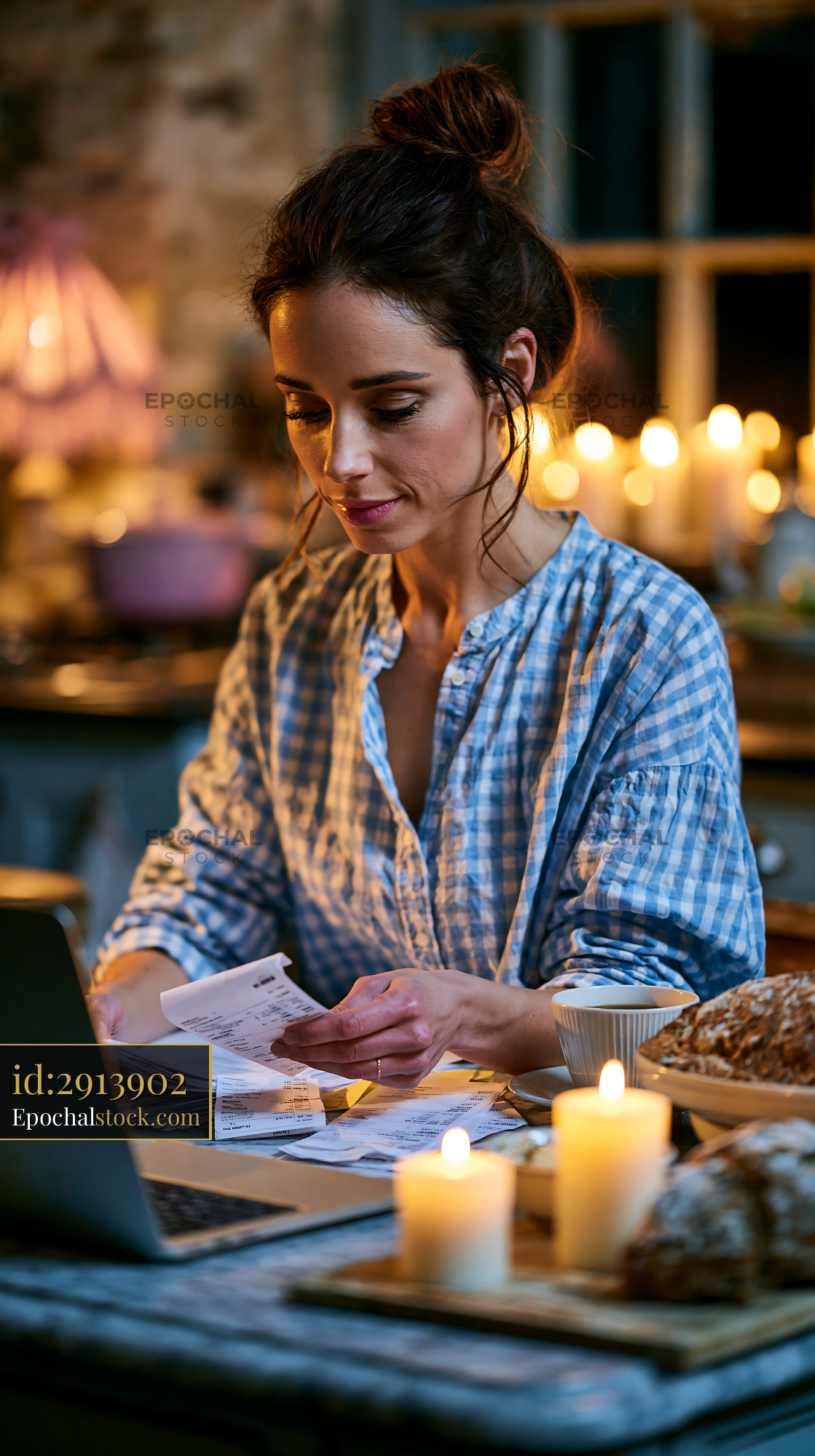 Watermarked full-resolution preview of Woman organizing bills at a desk with candles lit in the background