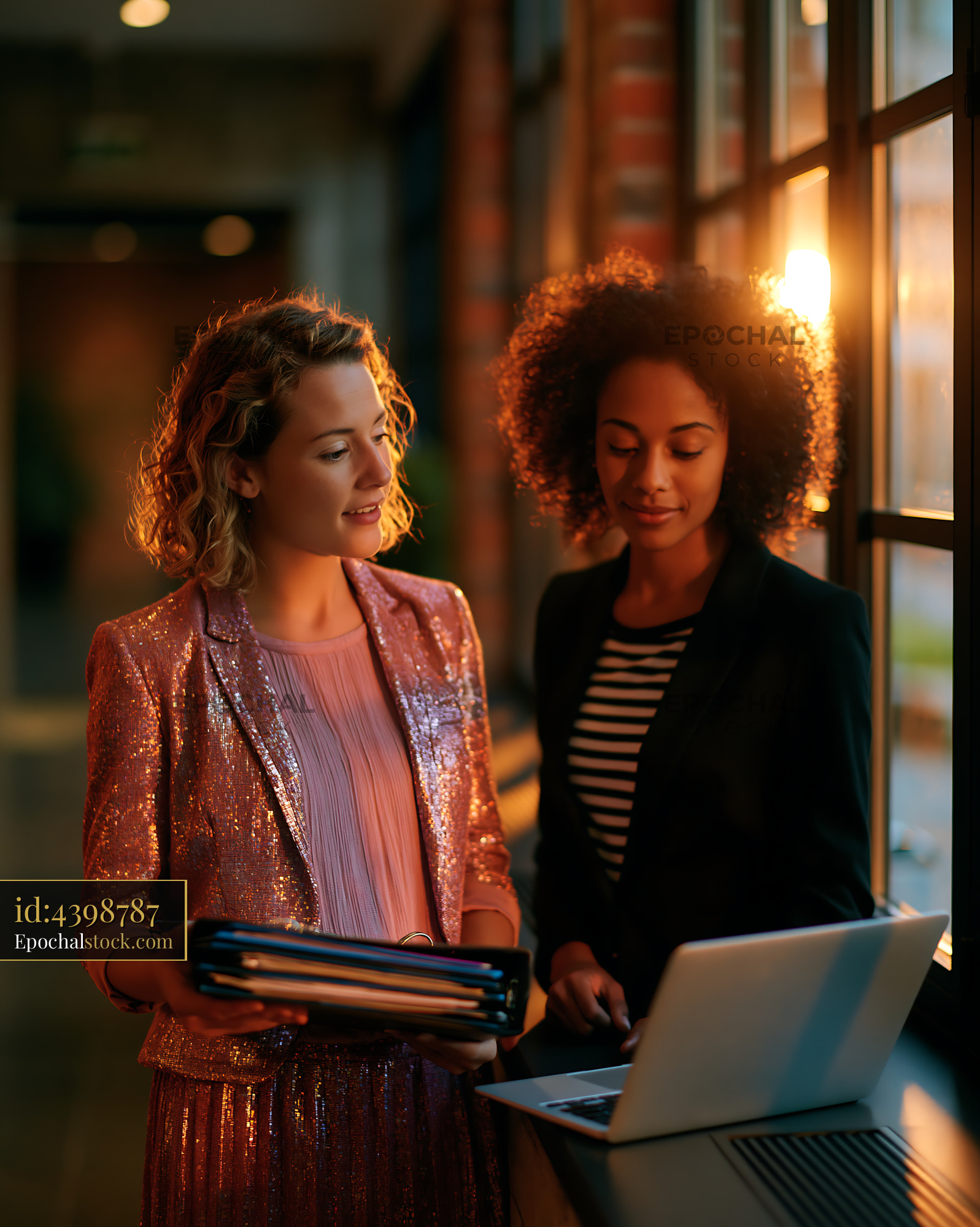 Watermarked full-resolution preview of Two women discussing work near a window during sunset