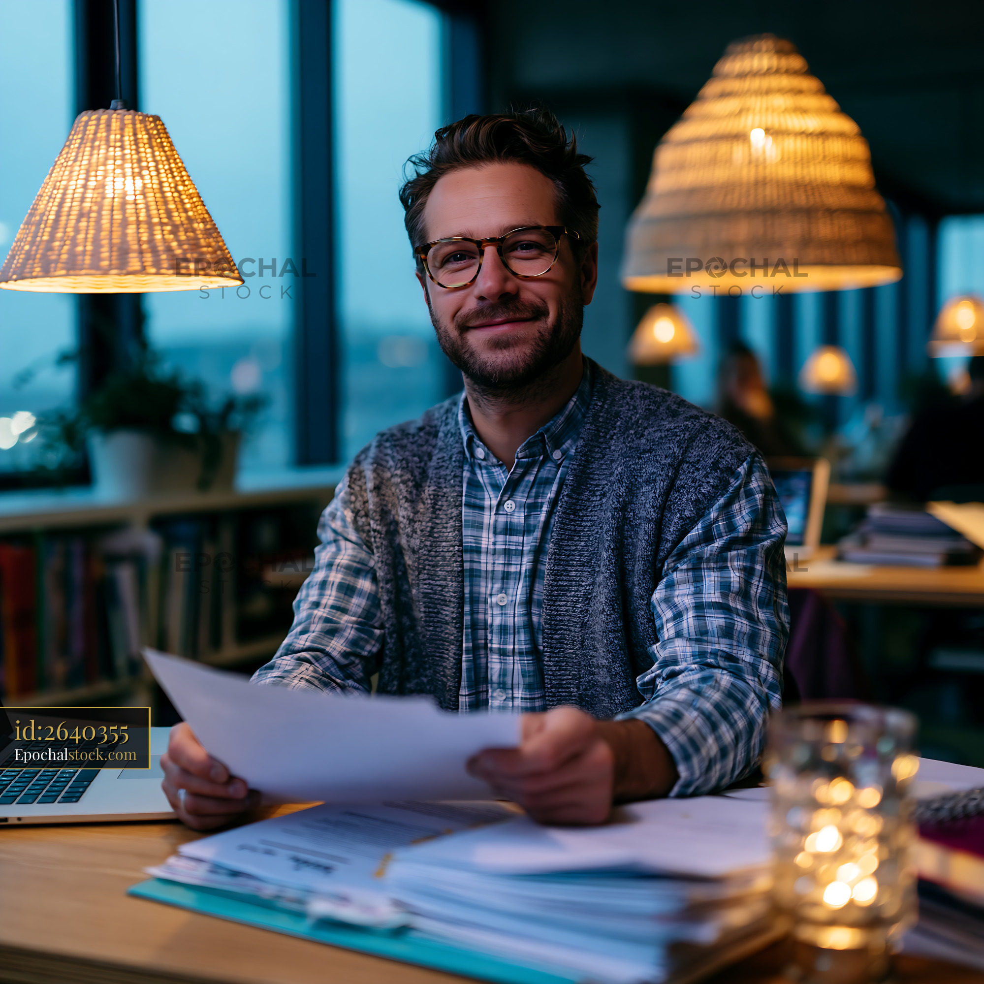 Watermarked full-resolution preview of Man working at a desk with papers and a laptop in a cafe