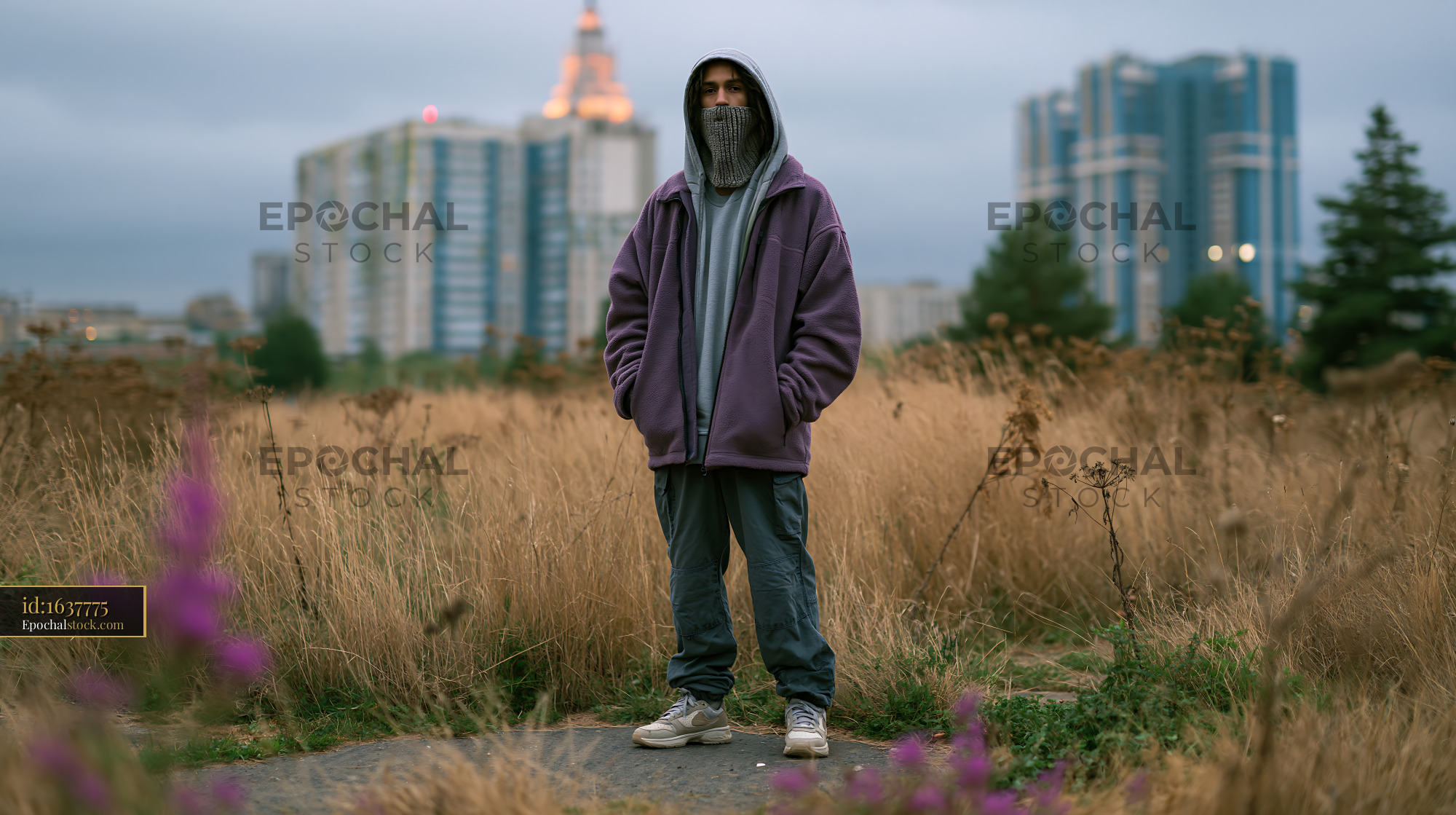 Watermarked full-resolution preview of Person in a field of tall grass with buildings behind