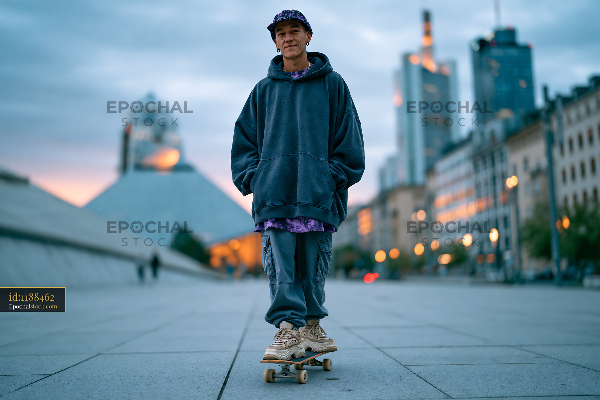Watermarked full-resolution preview of Skateboarder stands on skateboard in urban area at dusk
