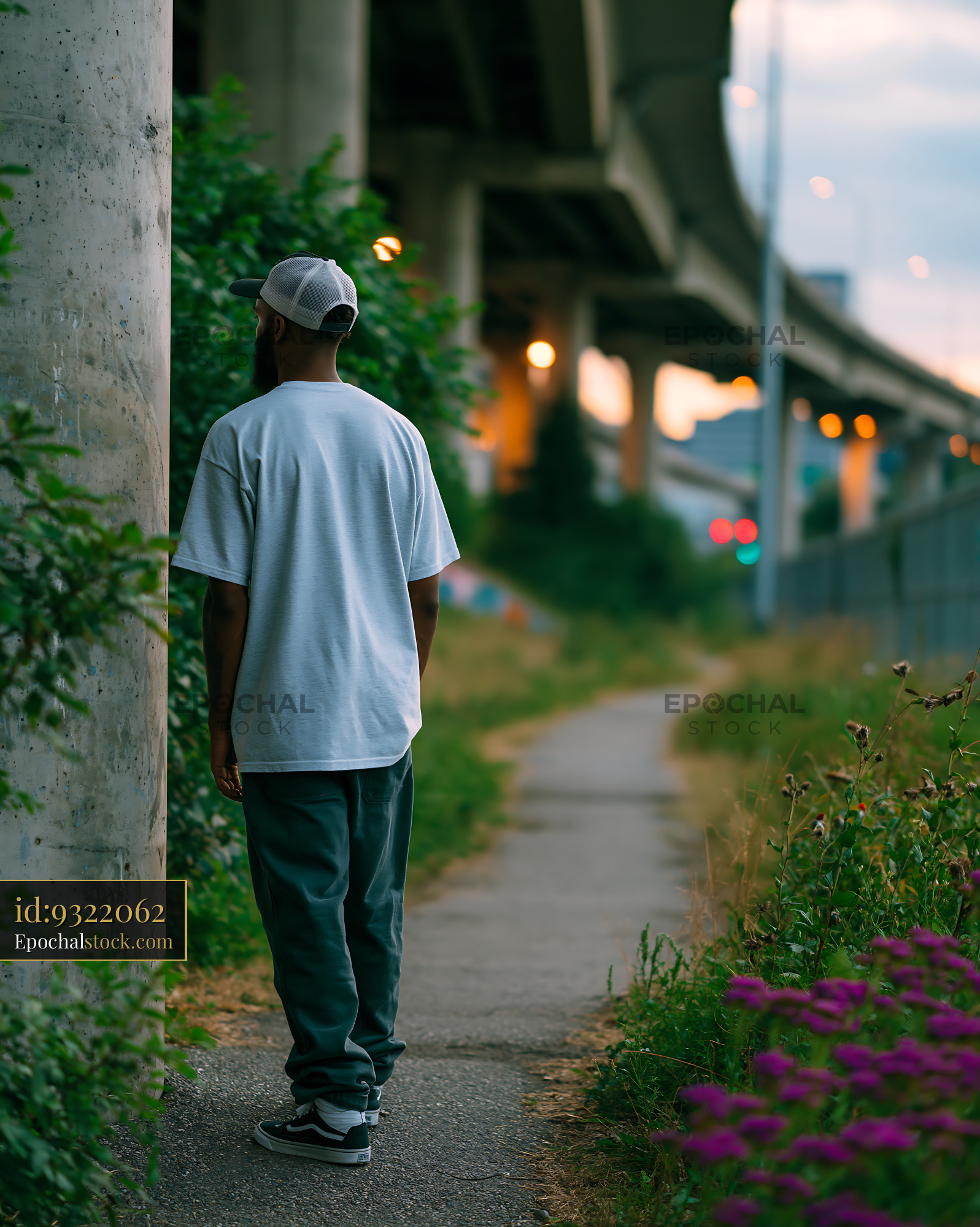 Watermarked full-resolution preview of Man walking on a path near a highway overpass at dusk