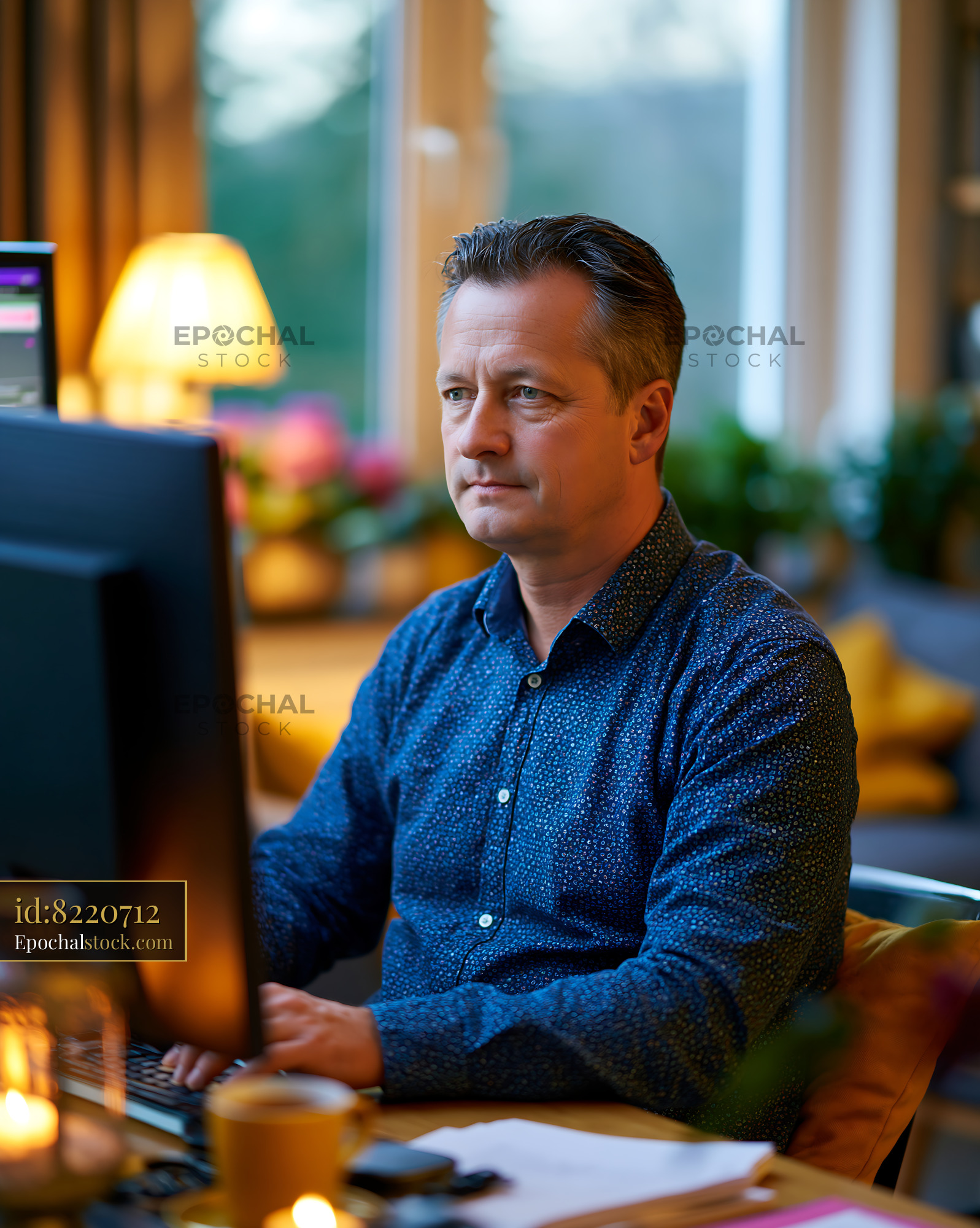 Watermarked full-resolution preview of Man working at a desk with a computer in a well-lit room