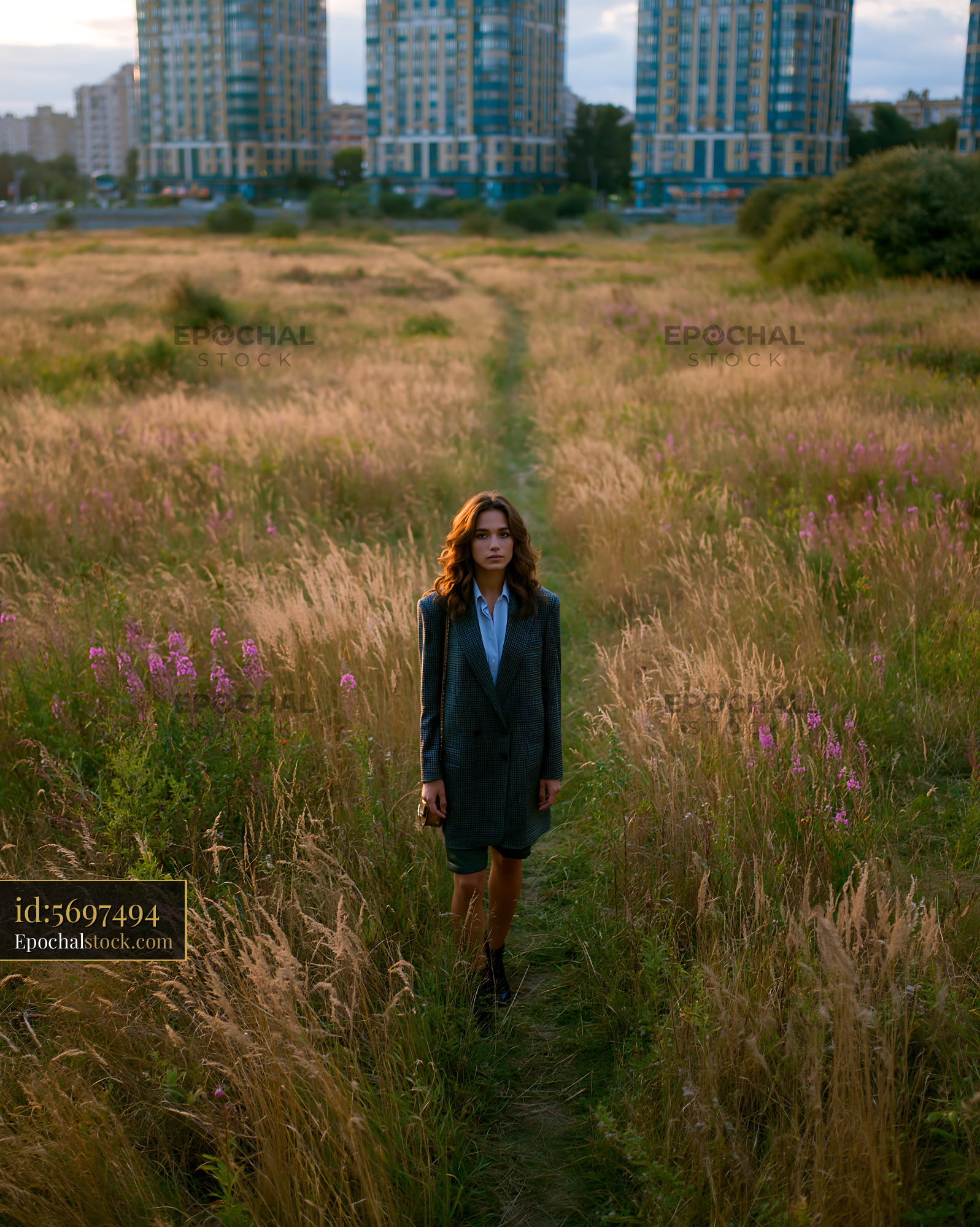 Watermarked full-resolution preview of Woman walking on path through tall grass near buildings