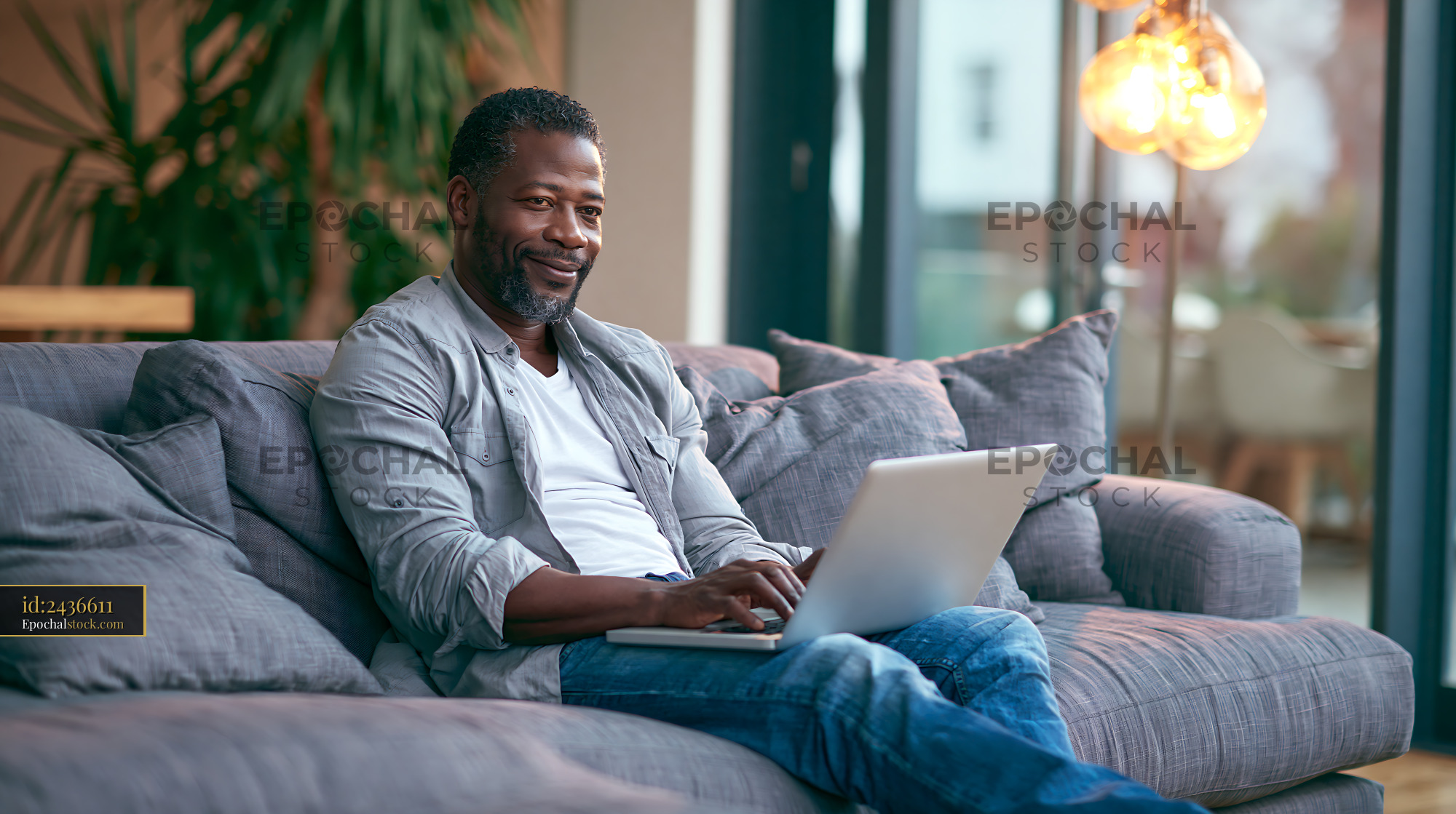 Watermarked full-resolution preview of Man working on laptop while sitting on a couch in a modern living room