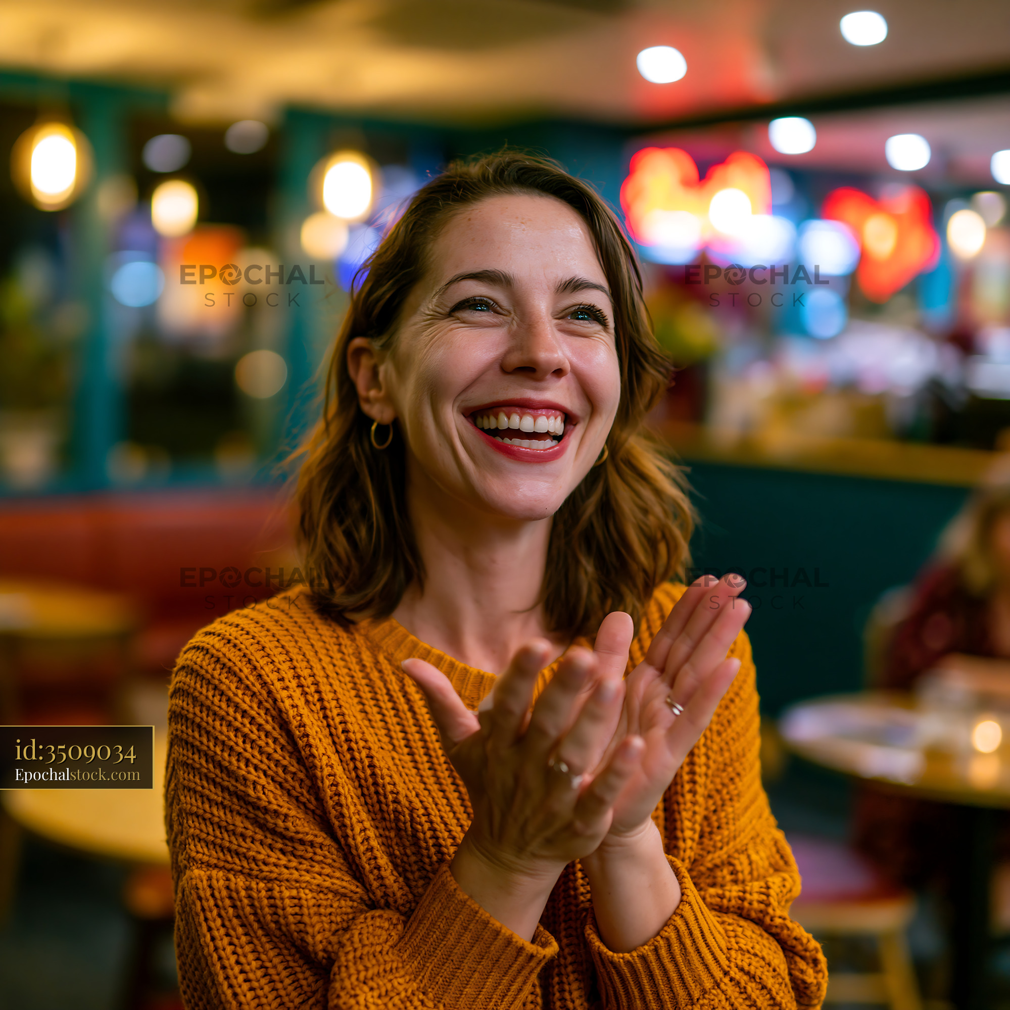 Watermarked full-resolution preview of Woman clapping and smiling in a cozy diner setting at night