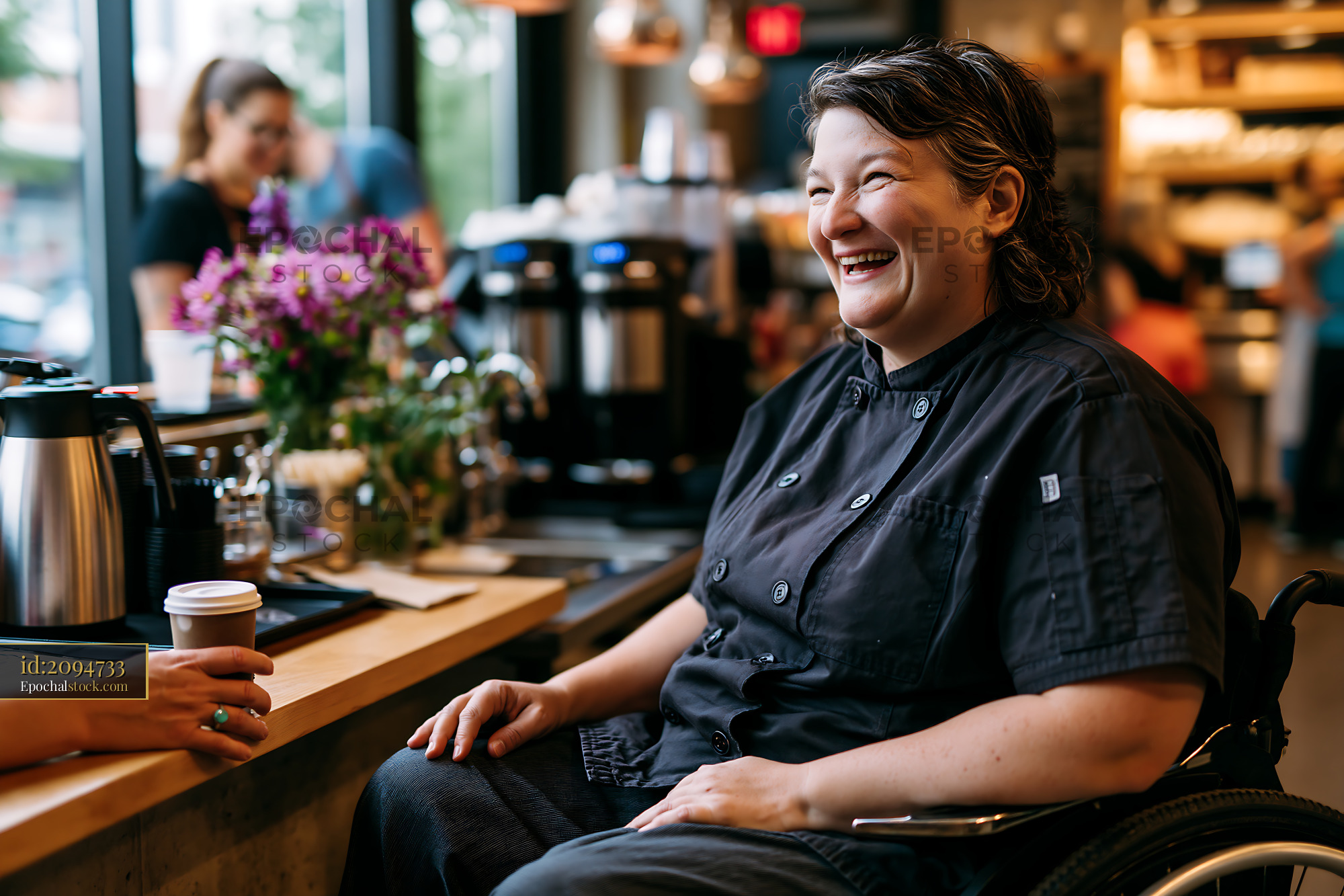 Watermarked full-resolution preview of Smiling barista in wheelchair interacting with customers in cafe