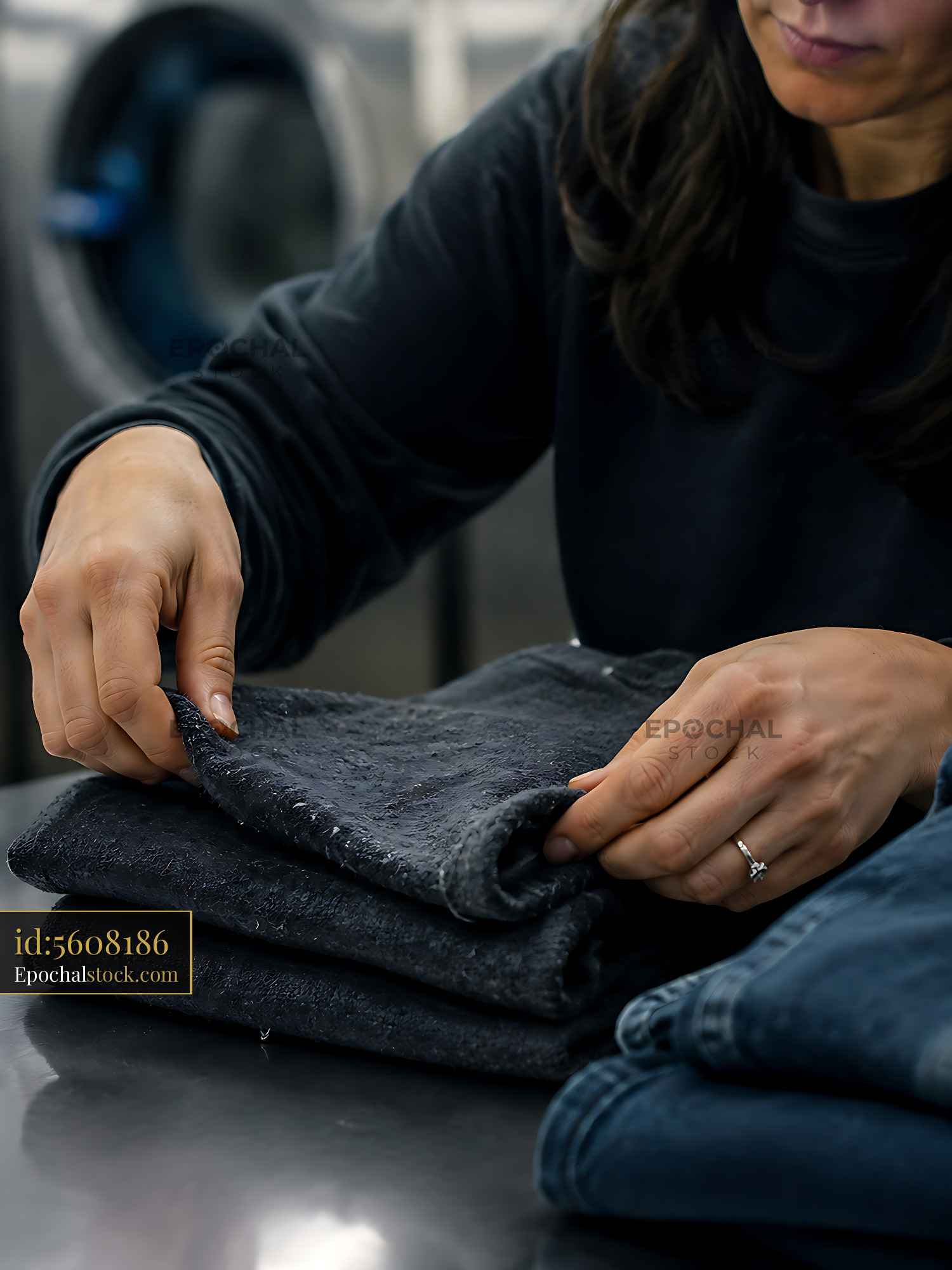 Watermarked full-resolution preview of Woman folding clothes in a laundry facility