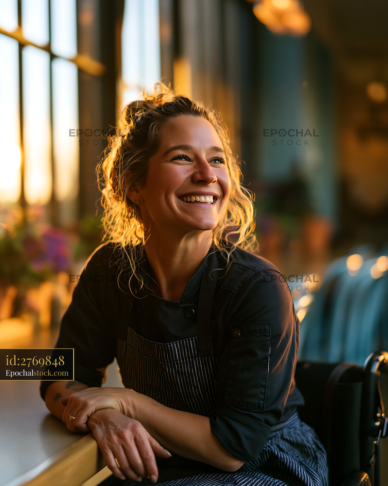 Watermarked full-resolution preview of Smiling woman wearing an apron works at a cafe in the evening
