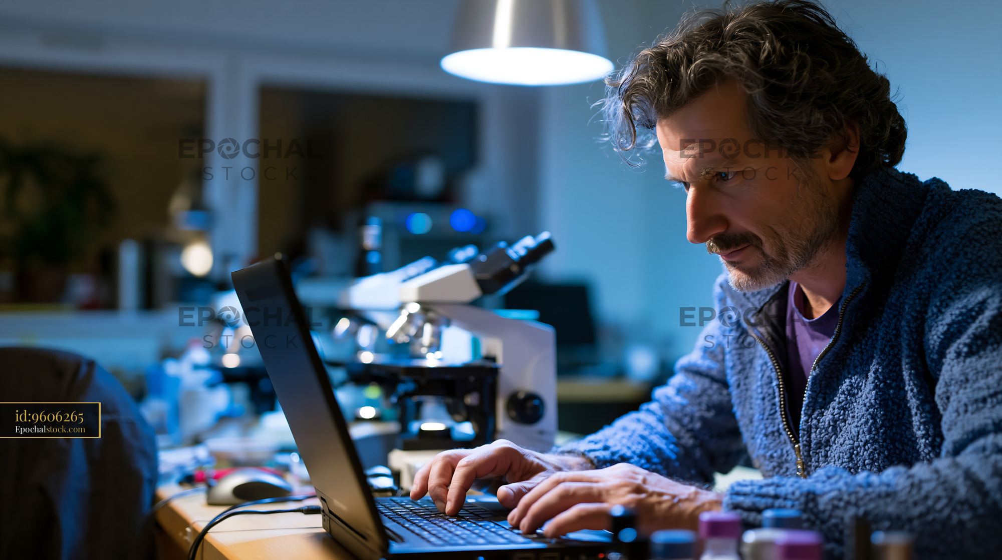 Watermarked full-resolution preview of Researcher working at a desk with laptop and microscope