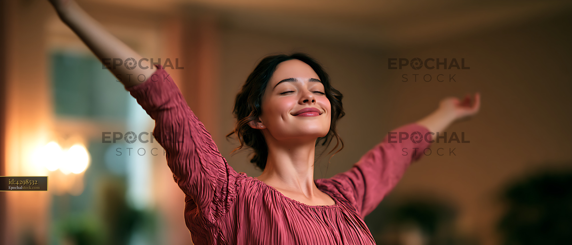 Watermarked full-resolution preview of Happy woman celebrating with arms outstretched indoors