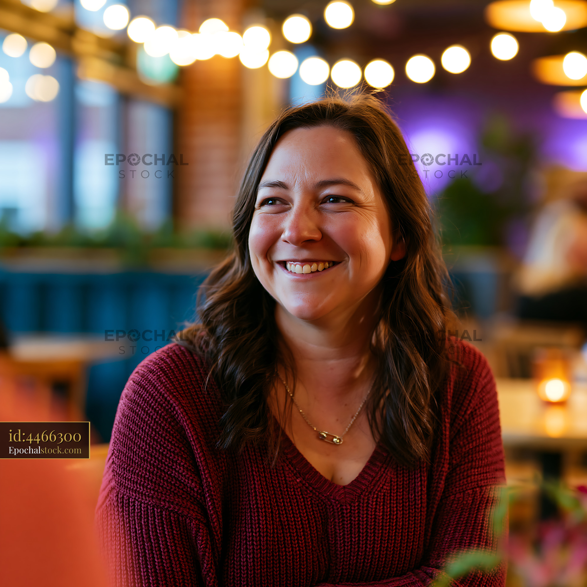 Watermarked full-resolution preview of Woman smiles while sitting in a restaurant with warm lighting